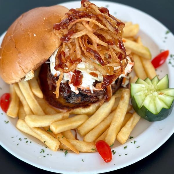 A Michigan Deli burger with crispy onions, BBQ sauce, and coleslaw, served with fries and cucumber.