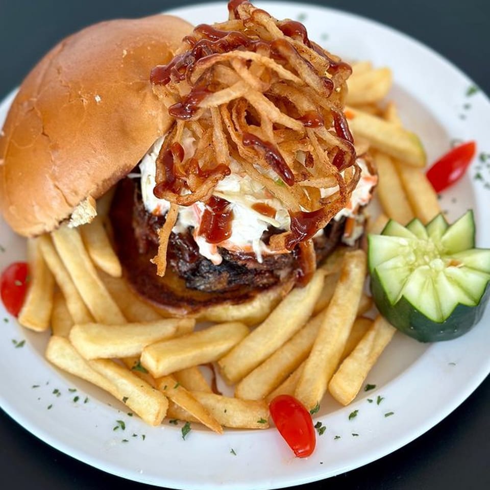 A Michigan Deli burger with crispy onions, BBQ sauce, and coleslaw, served with fries and cucumber.