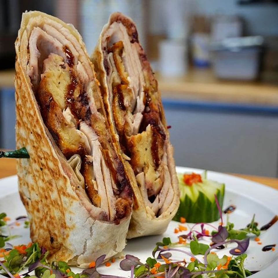 A Michigan Deli wrap, sliced in half, revealing turkey, stuffing, and gravy, garnished with microgreens.