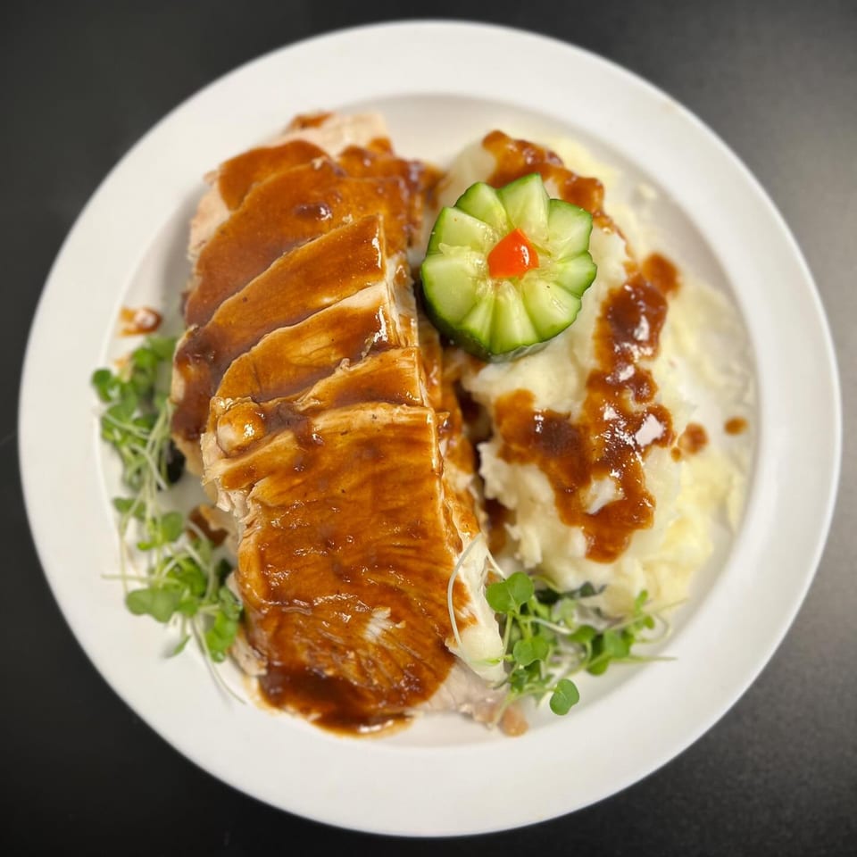 Sliced turkey with gravy, mashed potatoes, and a cucumber garnish on a white plate.