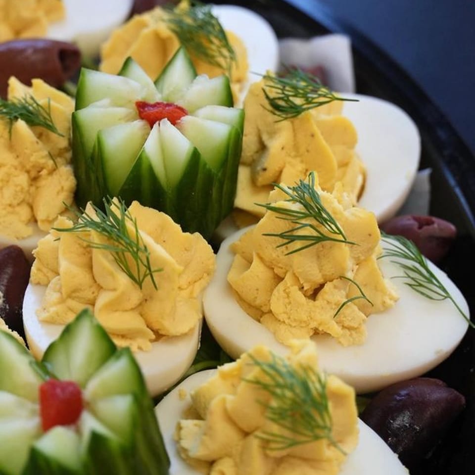 Deviled eggs with dill and cucumber garnishes, alongside dark olives on a platter.