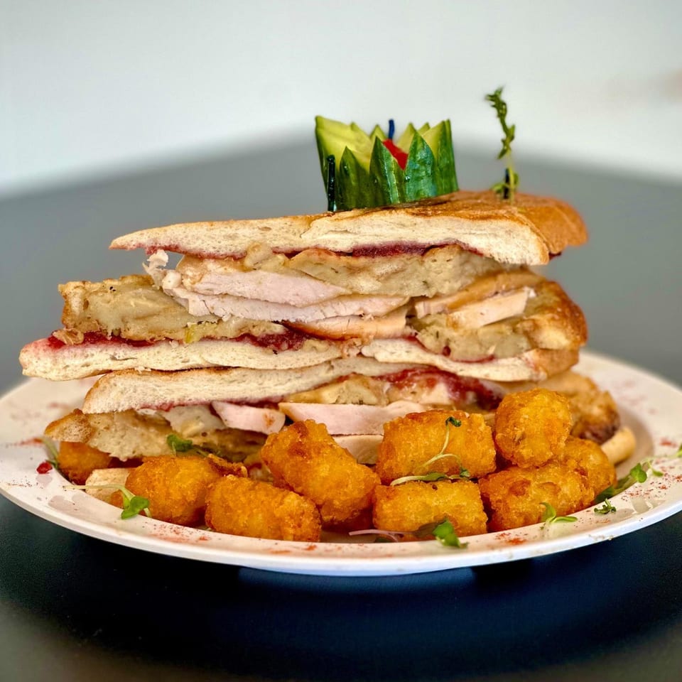 Towering deli sandwich with turkey, cranberry sauce, and stuffing, served with tater tots.